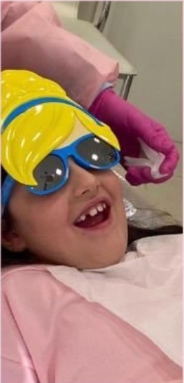 Criança sorrindo com óculos de proteção durante atendimento odontopediátrico