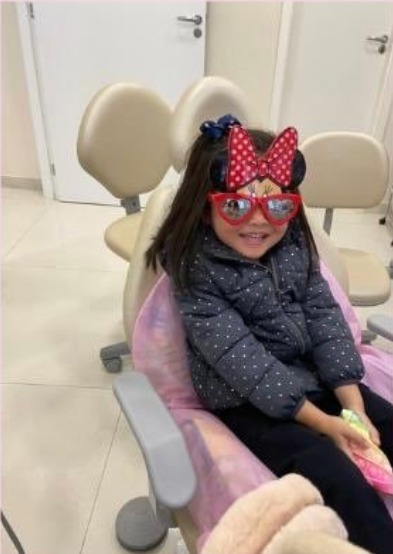 Menina sentada na cadeira odontológica em consultório de odontologia infantil